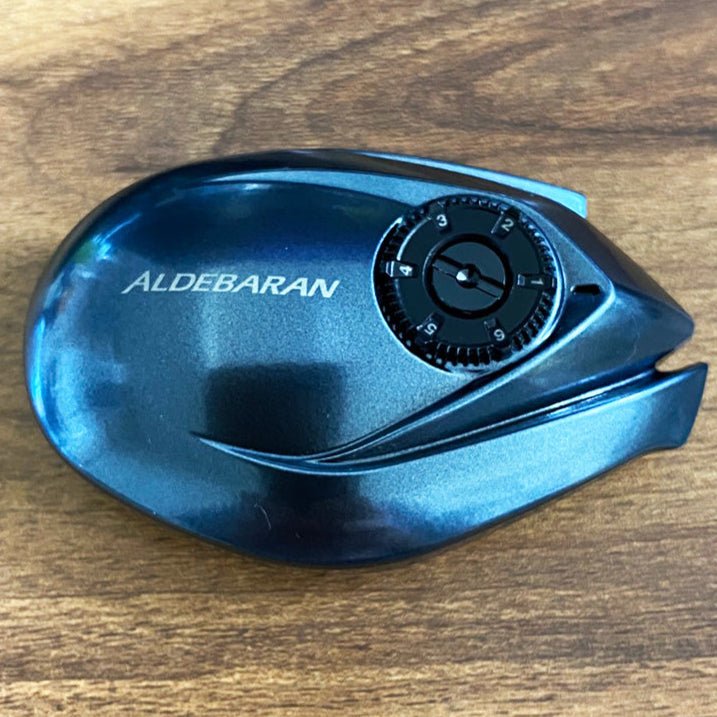 Eine Nahaufnahme der Hedgehog Studio Brake Dial Screw für Shimano 22 Aldebaran BFS - Farb-Tuning für die Bremsverstellung mit nummeriertem Einstellrad wird auf einer Holzoberfläche gezeigt.