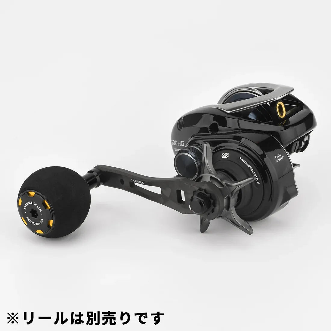 Eine schwarze Angelrolle mit einem Gomexus Forged Carbon Handle 65-75 mm mit EVA Power Knob und goldenen Akzenten ist auf weiΓem Hintergrund abgebildet. Der Markenname Gomexus und ein japanischer Text sind in der unteren linken Ecke sichtbar.