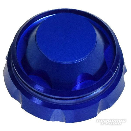 Ein metallisch blauer, runder Hedgehog Studio Griff-Schraubverschluss mit Rillen und glatter, flacher Oberseite ist schräg auf weißem Hintergrund abgebildet. Das Hedgehog Studio-Logo erscheint in der unteren rechten Ecke.