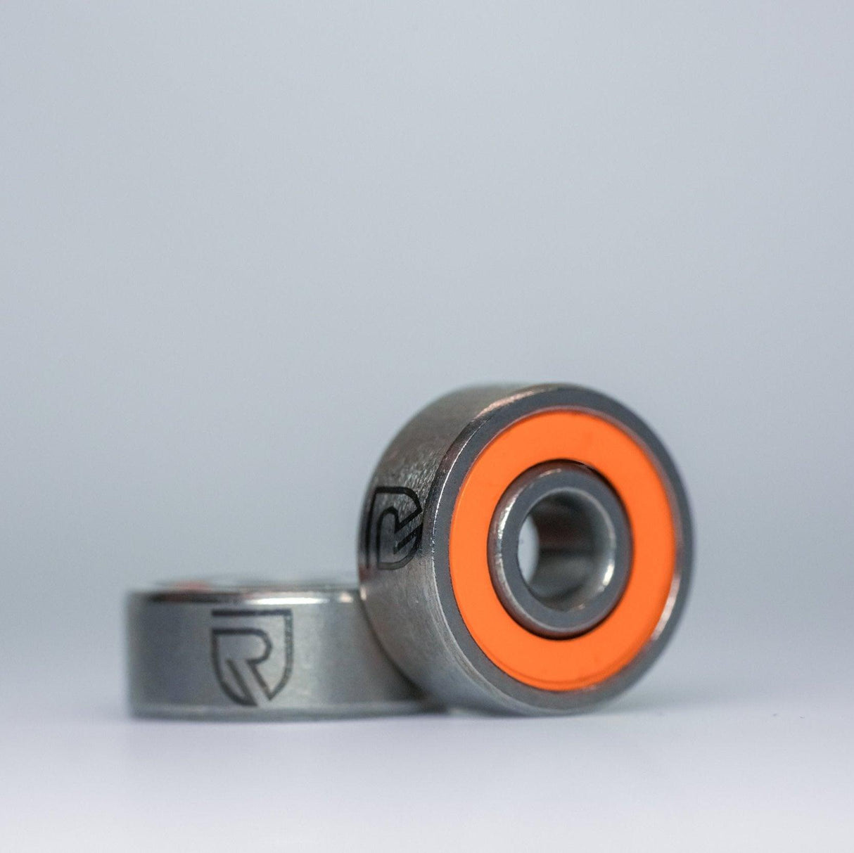 Zwei RL-TNG Hybrid Keramik Kugellager von RL-Angelrollentuning, ABEC 9, werden mit orangefarbenen Dichtungen β eine stehende und eine flache β gezeigt, ideal fΓΌr das Tuning von Baitcaster-Angelrollen. Beide Lager zeigen das in das MetallgehΓ€use eingeΓ€tzte Logo.