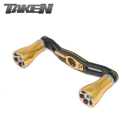 Der Taken A2 Carbon Griff 90 mm verfügt über zwei goldene Aluminiumknöpfe und einen metallischen A2 Carbonrahmen, der für Shimano & Daiwa Spinn- oder Baitcaster-Rollen entwickelt wurde. Das TAKEN-Logo erscheint in der oberen linken Ecke.