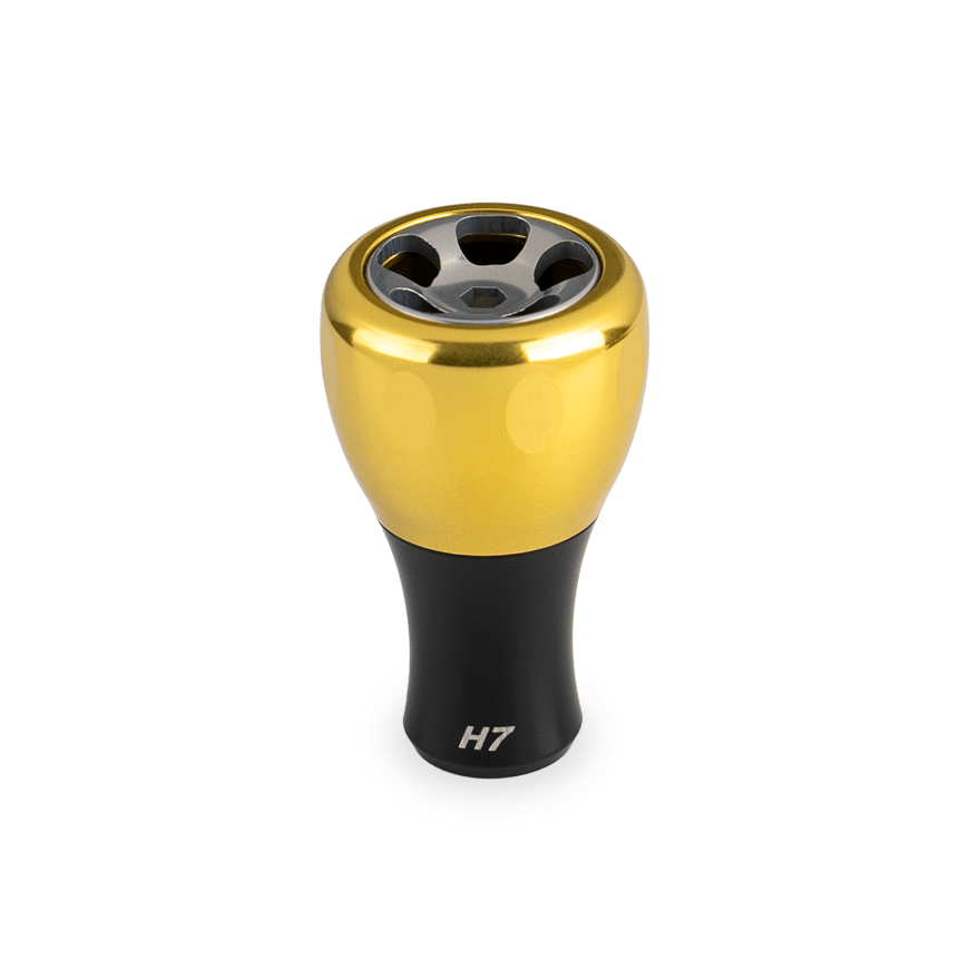 Ein Taken H7 Knopf 40mm von Taken, in Soft Gold mit schwarzem Sockel und "H7" Markierung, entwickelt für das Tuning von Shimano & Daiwa Baitcaster oder Spinnrollen, wird auf einem weißen Hintergrund gezeigt.