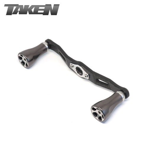 Der Taken One11 A2 Carbon Griff 111 mm in gunmetal mit zwei A2 Aluminium Knöpfen für Shimano & Daiwa ist auf weißem Hintergrund abgebildet. Das Wort TAKEN erscheint in stilisierten Buchstaben oben links.