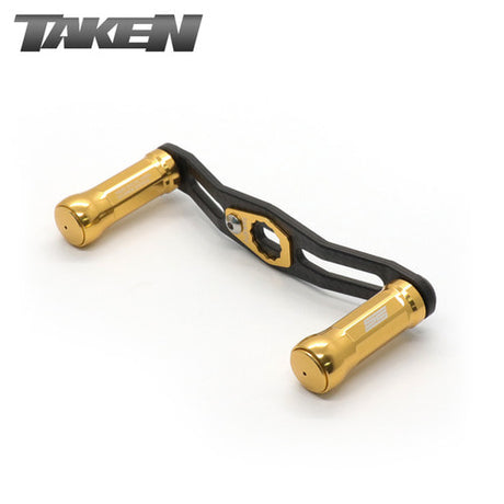 Ein goldener Taken SS Carbon Griff 85 mm mit zwei SS Aluminium Knöpfen für Shimano & Daiwa. Oben links ist "TAKEN" abgebildet und zeigt dieses fein abgestimmte Baitcaster-Zubehör.