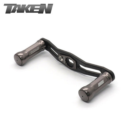 Der Taken SS Carbon Griff 85 mm in gunmetal verfügt über SS Aluminiumknöpfe und ist ideal für Shimano & Daiwa Finesse-Baitcaster Setups; der TAKEN Markenname erscheint in der oberen linken Ecke.