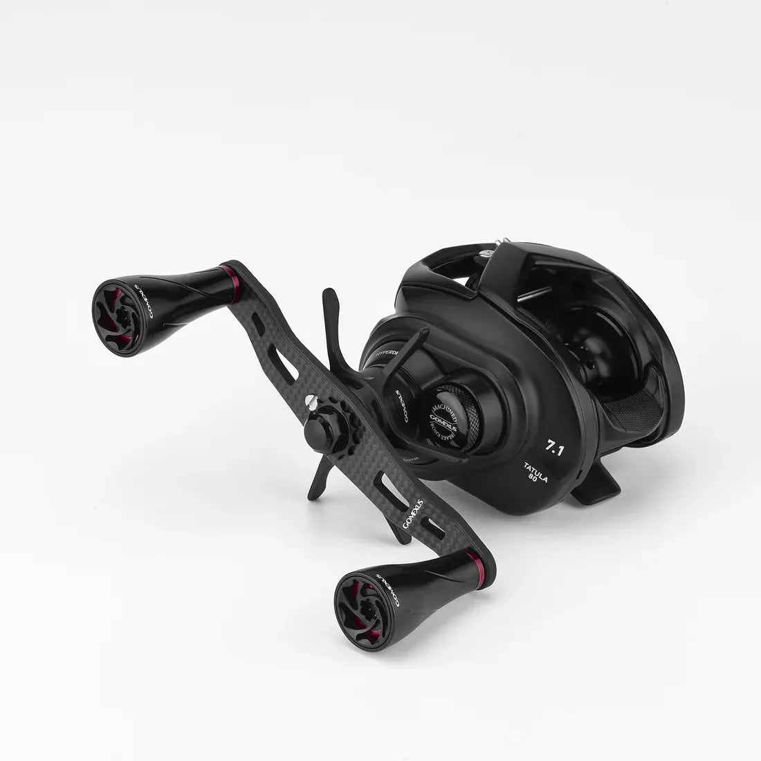 Eine schwarze Baitcasting-Rolle mit zwei Griffen, die mit dem Gomexus 95mm Carbon-Griff mit A20P-Knöpfen, einem sichtbaren Gang-Einstellknopf und einer 7,1-Gangkennzeichnung vor einem schlichten weißen Hintergrund ausgestattet ist. Marke: Gomexus.