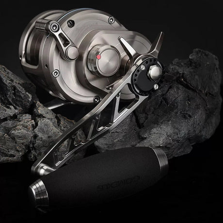 Nahaufnahme einer modernen, metallischen Angelrolle mit dem Gomexus Aluminiumgriff 95 mm und 85 mm T-Bar-Knauf (8 x 5 mm), dargestellt auf dunklem Felsen. Die Rolle hat eine matte Oberfläche, sichtbare Schrauben und ein industrielles Design. Marke: Gomexus.