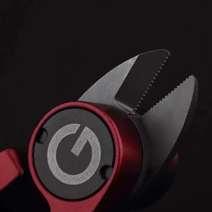 Eine Nahaufnahme des Gomexus SharkBite Schnurknipser Combo von Gomexus mit gezackten Edelstahlklingen und einem kreisförmigen Symbol für den Einschaltknopf, dargestellt vor einem dunklen Hintergrund.