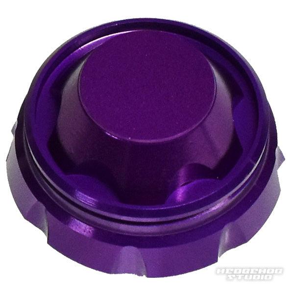 Ein metallisch-violetter, runder Hedgehog Studio Griff-Schraubverschluss mit Rillen und glänzender Oberfläche ziert einen weißen Hintergrund. Die erhabene Mitte verleiht ihm Stil, und das HEDGEHOG STUDIO Wasserzeichen erscheint in der unteren rechten Ecke.