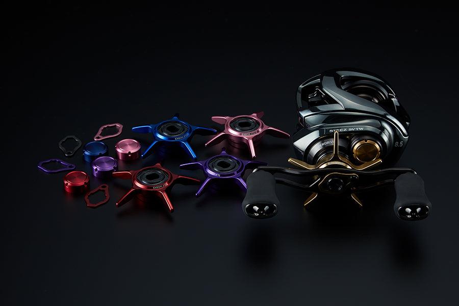 Der SLP Works 24 Steez SV TW SCL Star Drag von SLP Works wird mit zwei schwarzen Griffen, metallisch roten, blauen und rosafarbenen austauschbaren Star Drag-Teilen, passenden Kappen und Werkzeugen auf einer schwarzen Oberfläche präsentiert.