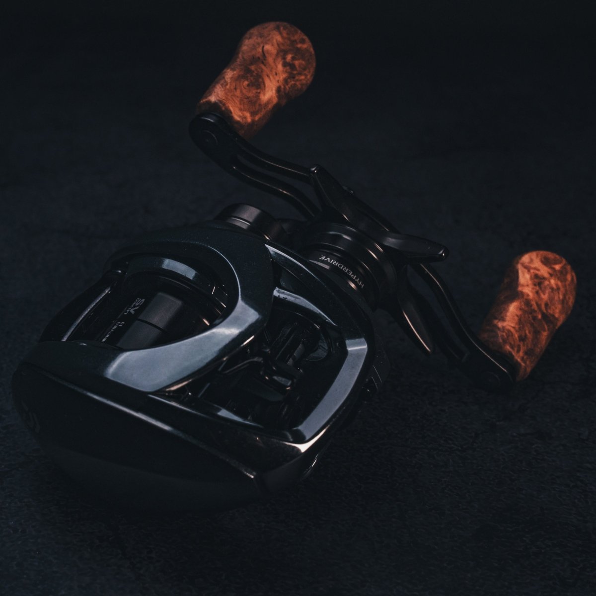 Nahaufnahme vom SLP Works i Shape Wood Knob Limited Edition – das schicke schwarze Baitcaster-Griffstück von SLP Works, perfekt zum Tunen deiner Angelrolle! Edler Holz-Knauf, frisches Design und mega Grip für extra Style am Wasser. Fotografiert vor dunklem Hintergrund, damit du jedes Detail siehst und direkt merkst: Damit hebst du dein Tackle auf’s nächste Level!.