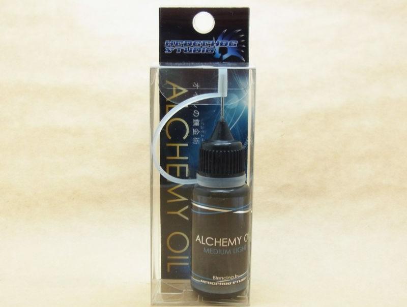 Eine kleine Flasche mit der Aufschrift „Hedgehog Studio Alchemy Oil Medium Light Rollenöl“ befindet sich in einer transparenten Verpackung mit schwarzem Tropfverschluss. Der Markenname Hedgehog Studio steht oben, ideal für Kugellagerpflege oder Angelrollenöl.