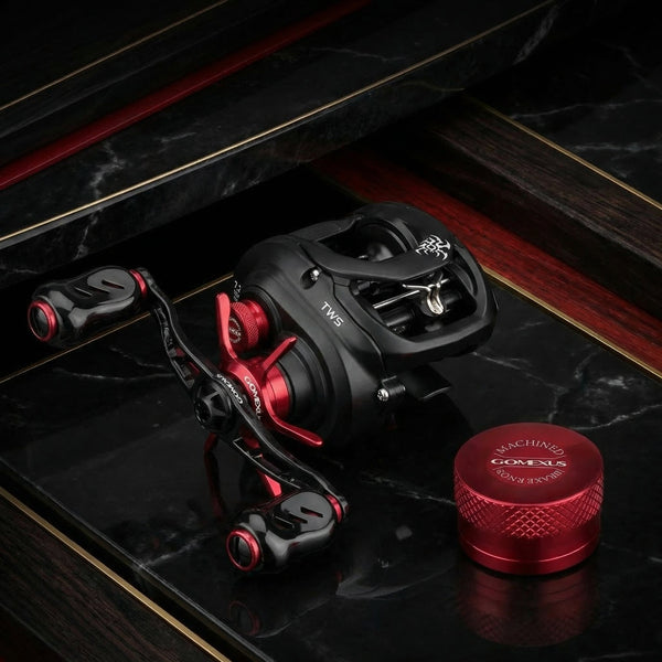 Nahaufnahme von zwei Angelrollen; die linke Rolle hat einen roten Knopf und ruht auf getrocknetem Gras, während die rechte Rolle einen violetten Knopf hat und teilweise in Wasser mit sichtbaren Wassertropfen getaucht ist.