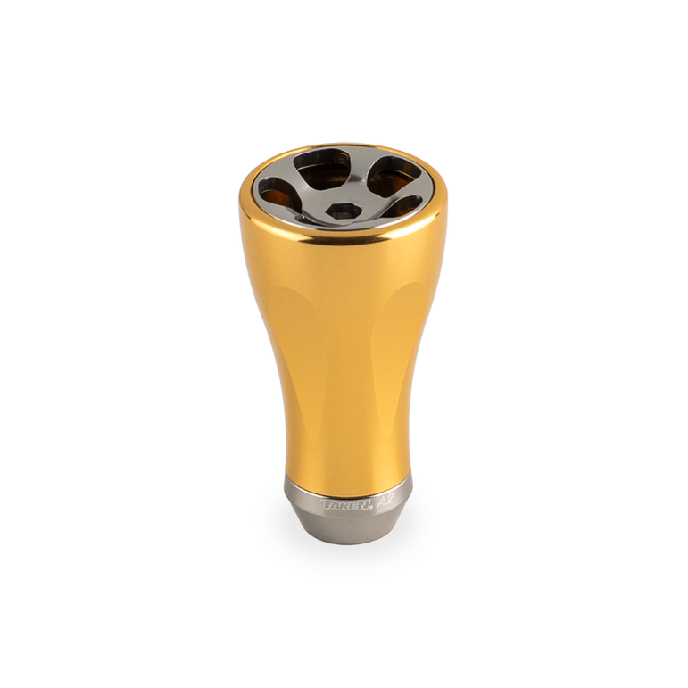 Der Taken A2 Knob 36mm ist ein gold-metallic Tuning-Aluminiumknopf für Shimano & Daiwa Rollen. Er ist aufrecht auf einem weißen Hintergrund mit vier kreisförmigen Öffnungen und einer polierten reflektierenden Oberseite abgebildet. Marke: Taken.