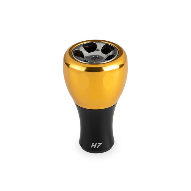 Der Taken H7 Knob 40mm von Taken ist ein goldener Aluminium-Stimmknopf für Baitcaster und Spinnrollen (Shimano und Daiwa). Er hat eine metallische Oberfläche mit vier kreisförmigen Aussparungen und einer "H7"-Markierung auf weißem Hintergrund.