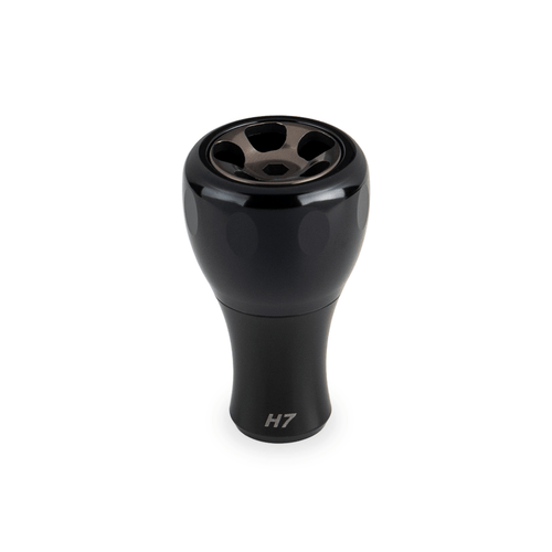Ein schwarzer Taken H7 Knob 40mm - Aluminium Tuning Knauf, entworfen für Shimano & Daiwa Baitcaster und Spinnrollen, wird vor einem weißen Hintergrund gezeigt. Die metallisch glänzende Oberseite weist fünf kreisförmige Öffnungen und ein Branding im unteren Teil auf.