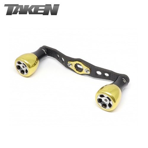 Der Taken H7 SS Crossover Carbon Griff 100 mm mit weichen goldenen H7 Aluminiumknöpfen für Shimano und Daiwa Rollen zeigt das TAKEN Logo in der oberen linken Ecke auf weißem Hintergrund.