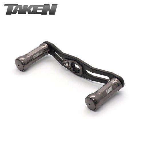 Der Taken SS Carbon Griff 85 mm in gunmetal verfügt über SS Aluminiumknöpfe und ist ideal für Shimano & Daiwa Finesse-Baitcaster Setups; der TAKEN Markenname erscheint in der oberen linken Ecke.