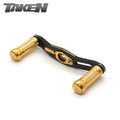 Ein Taken SS Carbon Handle 90 mm mit SS Aluminium Knöpfen, entworfen für Shimano & Daiwa Baitcaster Rollen, ist in Gold auf weißem Hintergrund abgebildet. Der Markenname TAKEN erscheint in der oberen linken Ecke in silberner und schwarzer Schrift.