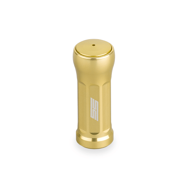 Der Taken SS Knob 35mm ist ein weicher, goldfarbener Aluminium-Stimmknopf für Shimano- und Daiwa-Rollen. Er verfügt über eine flache Oberseite mit zentralem Loch, seitlichen Rillen und einem weißen Logo - perfekt als Upgrade Baitcaster Rollen Knob. Abgebildet auf einem weißen Hintergrund.