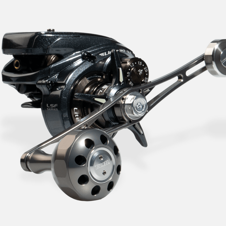 Eine Nahaufnahme des Taken X3 Knob 50mm von Taken, ein Power Tuning Griffknopf für Shimano & Daiwa Angelrollen (Hecht & Bigbait), zeigt metallische Ziffernblätter und komplizierte Teile vor einem schlichten hellen Hintergrund.