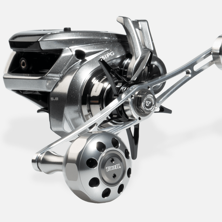 Eine Nahaufnahme zeigt den Taken X3 Knob 50mm Power Tuning Handle für Shimano & Daiwa Rollen, Marke Taken, mit einem großen perforierten Knopf für das Hecht & Bigbait Angeln, fotografiert vor einem schlichten weißen Hintergrund.