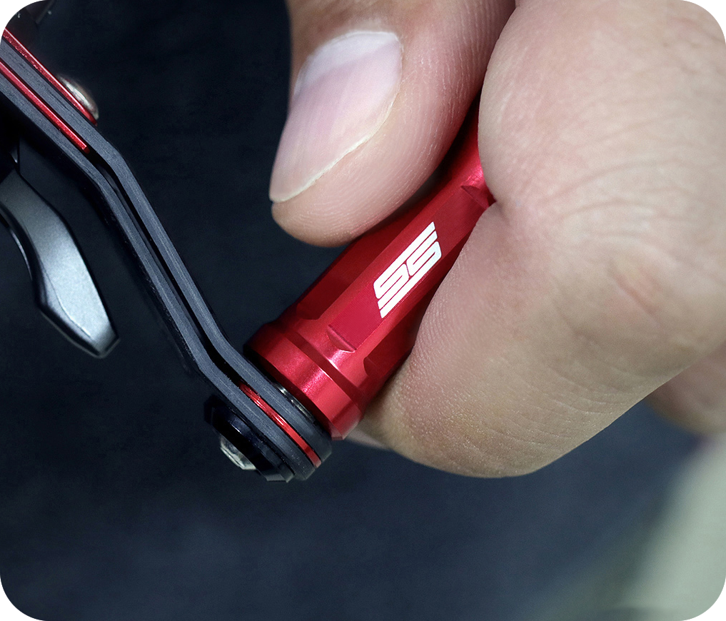 Eine Nahaufnahme zeigt eine Hand, die den 35mm Taken SS Knob greift, einen roten Tuning Aluminium Knauf für Shimano & Daiwa Angelrollen, mit weißer 