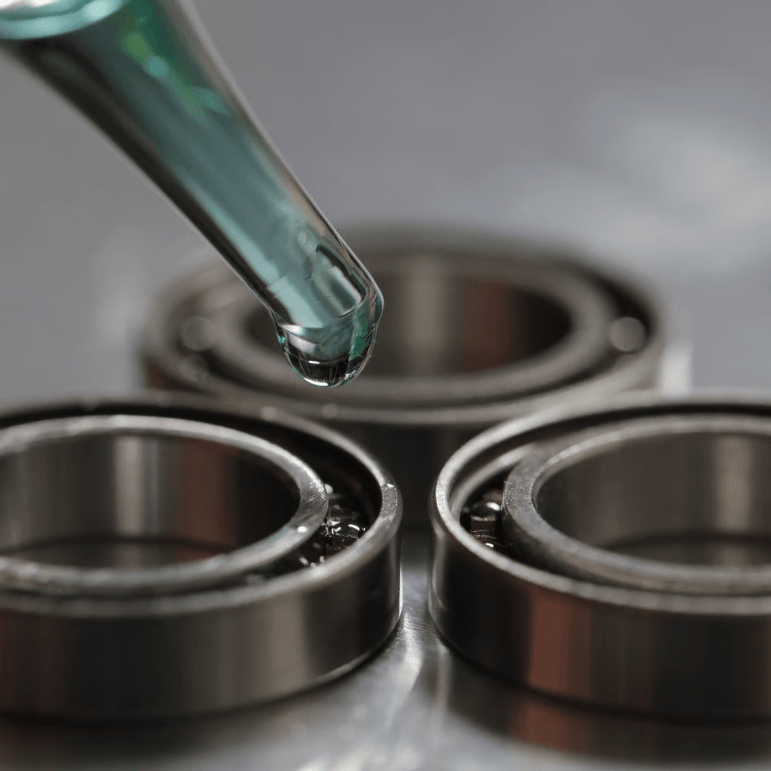 Eine Nahaufnahme einer Pipette, die Glitch Oil High Spec Bearing von Glitch Oil Japan auf Kugellager abgibt, die auf einer metallischen Oberfläche angeordnet sind.