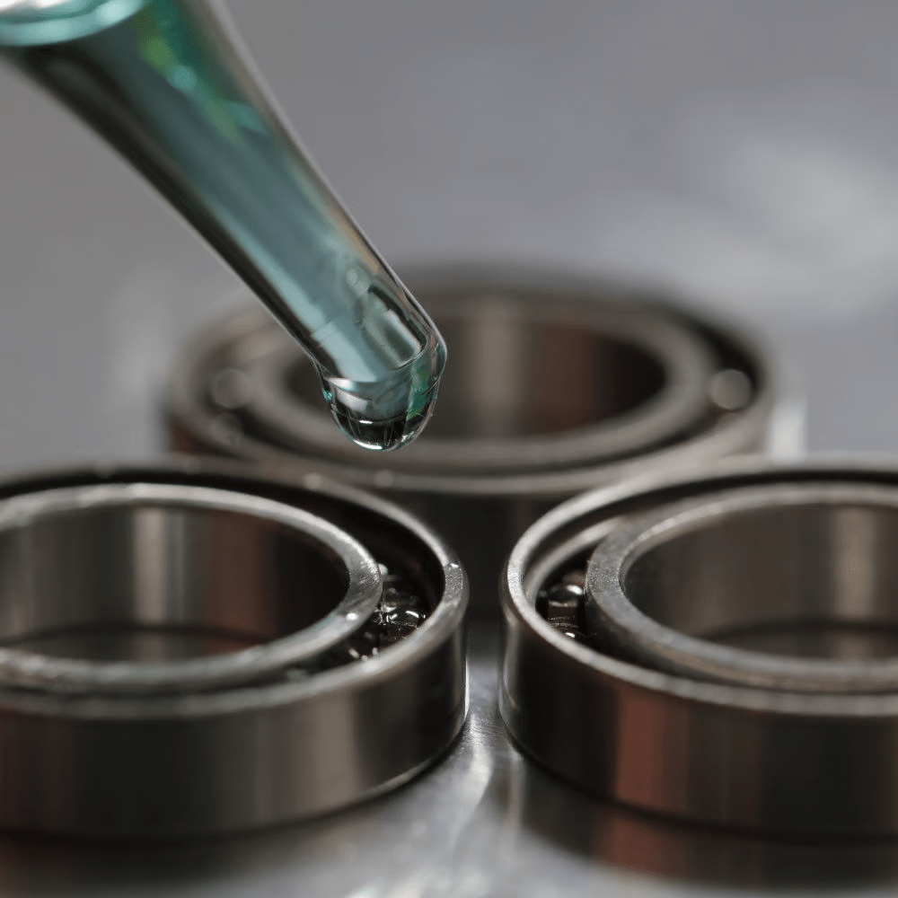 Eine Nahaufnahme einer Pipette, die Glitch Oil High Spec Bearing von Glitch Oil Japan auf Kugellager abgibt, die auf einer metallischen Oberfläche angeordnet sind.