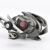 Eine Nahaufnahme einer Shimano Baitcaster HG-Rolle mit grauem Metallic-Finish, Metanium-Tuning und der Gomexus Aluminum Spool Tension Knob Cap (20/22/23 Metanium) in Rot sowie einem schwarz-silbernen Griff auf weißem Hintergrund.