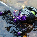 Eine Nahaufnahme einer Gomexus Aluminium-Spulenspannungsknopfkappe in Lila und Schwarz, die von Wassertropfen glitzert, während sie auf einer Angelrute ruht, die teilweise in seichtes Wasser eingetaucht ist.