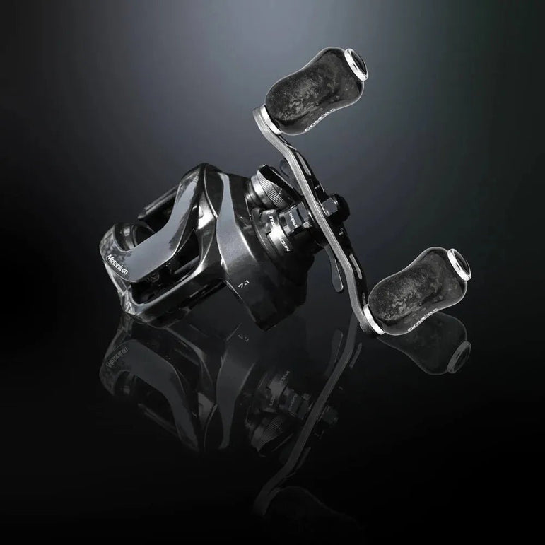 Eine schwarz-silberne Angelrolle mit zwei Griffen, die mit dem Gomexus Carbon Forged F22 Knob von Gomexus ausgestattet ist, wird auf einer dunklen, reflektierenden Oberfläche in einem Winkel angezeigt - ideal für ermüdungsfreies Angeln.