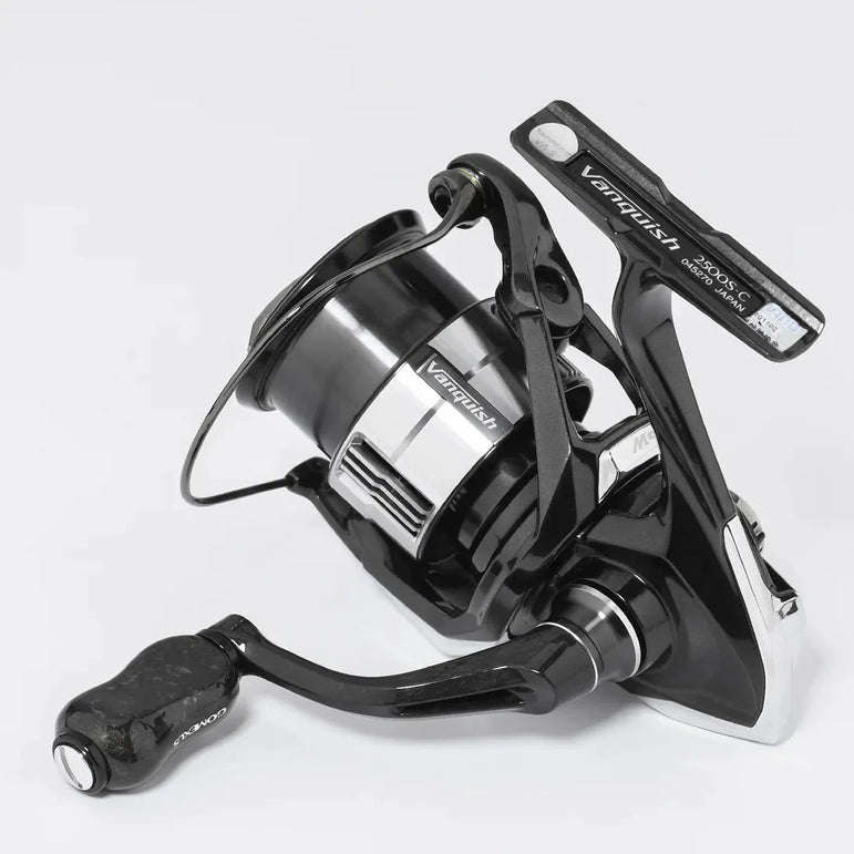 Eine schwarz-silberne Angelrolle mit einem Gomexus Carbon Forged F22 Knopf für ermüdungsfreies Angeln ist auf einem schlichten weißen Hintergrund abgebildet. Der Markenname Gomexus erscheint in weißer Schrift auf mehreren Teilen der Rolle.