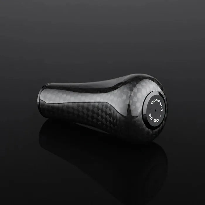 Ein schwarzer, strukturierter Gomexus FA30 Carbon-Knopf von Gomexus aus hochwertigem Toray-Carbon sitzt auf einer glänzend schwarzen Oberfläche. Weiße Markierungen und Zahlen auf der Oberseite weisen auf die Kompatibilität mit 5-Gang-Schaltgetrieben hin.