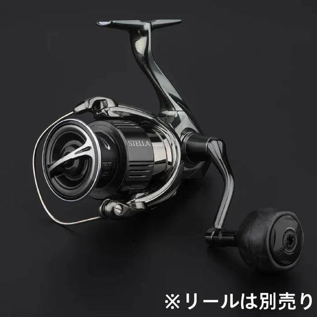 Nahaufnahme einer schwarz-silbernen Angelrolle mit dem Gomexus FA38S Carbon Knob 38 mm vor schlichtem schwarzem Hintergrund. Japanischer Text unten rechts weist darauf hin, dass die Rolle separat erhältlich ist.