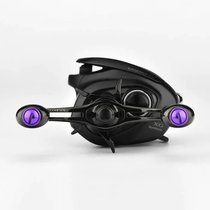 Eine schwarze Shimano-Baitcastingrolle mit metallisch-violetten Akzenten, ausgestattet mit dem Gomexus Kage Titanium Handle mit 22 mm Titanium Knobs (8 x 5 mm), ultraleichtes Angelzubehör von Gomexus, präsentiert vor einem schlichten weißen Hintergrund.