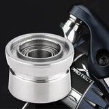Nahaufnahme eines silbernen Gomexus Schnurlaufröllchens für Shimano SW Angelrollen, vor einer teilweise sichtbaren dunklen Angelrolle mit der Aufschrift „PROTECT“, die den Spulenteil und die detaillierten Gomexus-Rollenkomponenten hervorhebt.
