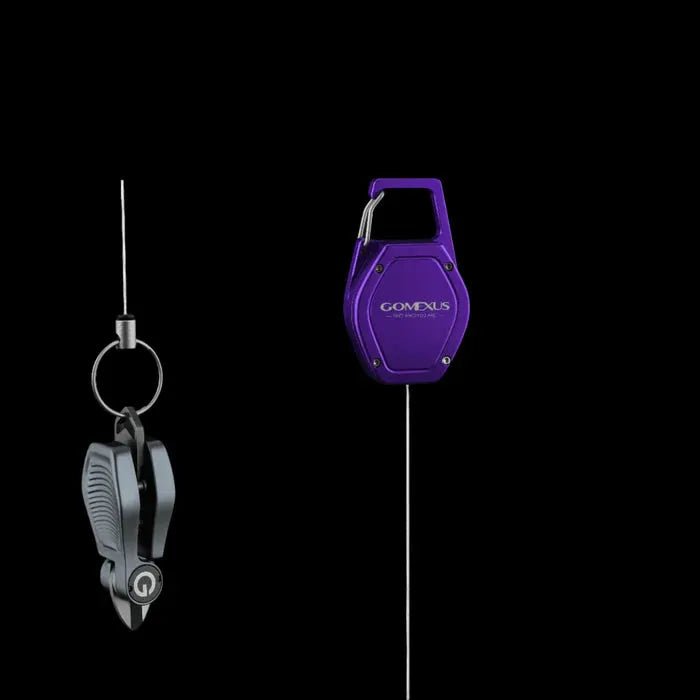 Die Gomexus SharkBite Schnurknipser Combo ist auf schwarzem Hintergrund abgebildet: das linke Werkzeug ist schwarz-silbern mit Clip, Ring und Klingen aus rostfreiem Stahl, während das rechte dreieckig, lila und mit dem Gomexus SharkBite Logo versehen ist.