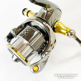 Nahaufnahme einer metallischen Hedgehog Studio Extra Super Duralumin Schraube für Schnurlaufröllchen mit goldenen und silbernen Akzenten vor einem schlichten weißen Hintergrund. Das Hedgehog Studio-Logo ist in der unteren rechten Ecke sichtbar.