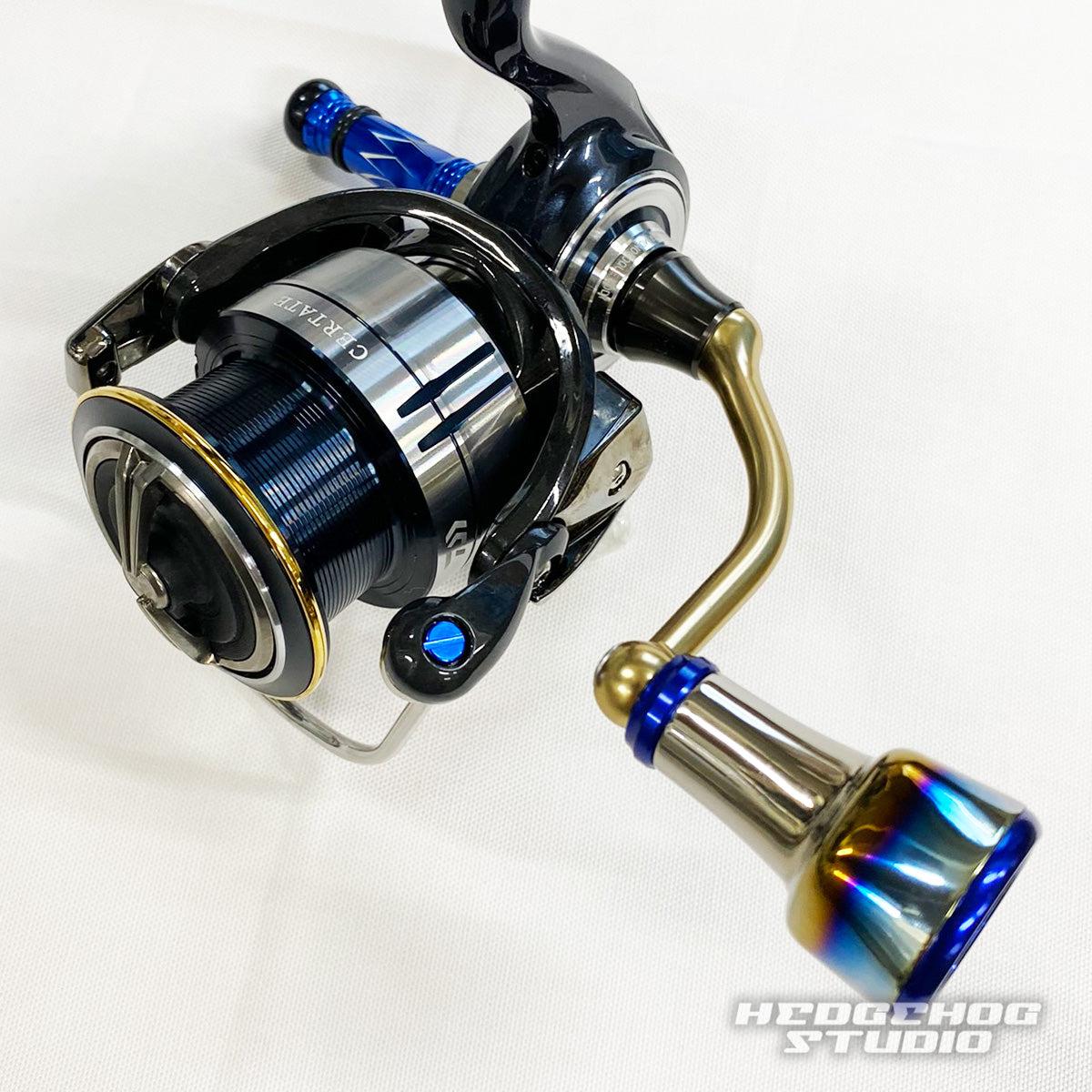 Eine Nahaufnahme der Hedgehog Studio Extra Super Duralumin Schraube für Schnurlaufröllchen mit metallisch blauen und goldenen Details auf einer Angelrolle, platziert auf einer weißen Oberfläche mit dem Hedgehog Studio-Logo in der unteren rechten Ecke.