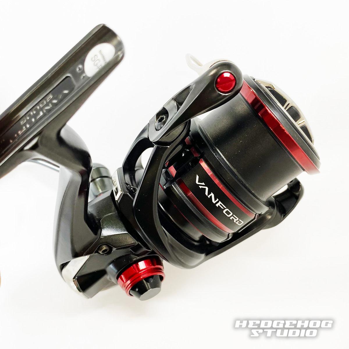 Nahaufnahme einer schwarz-roten Spinnrolle mit der Hedgehog Studio Extra Super Duralumin Schraube für Schnurlaufröllchen. Detaillierte Metallteile und das Hedgehog Studio-Logo sind in der unteren rechten Ecke sichtbar.