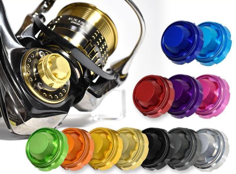 Eine Nahaufnahme einer Angelrolle mit einer goldenen Spule und einem Griff aus Duraluminium, zehn bunten Ersatzknöpfen und einer Schraubkappe für den Griff von Hedgehog Studio.