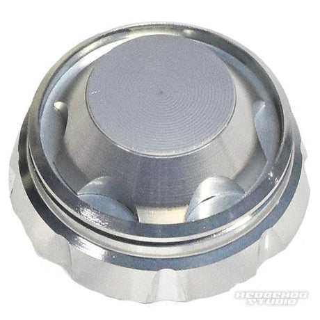 Eine Nahaufnahme des Schraubverschlusses von Hedgehog Studio mit rundem silbernem Design, strukturiertem Rand und flacher Oberseite auf weißem Untergrund. Das Hedgehog Studio-Logo befindet sich in der unteren rechten Ecke.