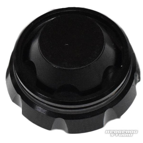 Auf weißem Hintergrund ist ein schwarzer, runder Hedgehog Studio-Griffschraubverschluss aus Kunststoff mit geriffelten Kanten und flacher Oberseite abgebildet. In der unteren rechten Ecke ist das Hedgehog Studio-Logo zu sehen.