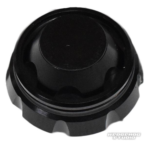 Auf weißem Hintergrund ist ein schwarzer, runder Hedgehog Studio-Griffschraubverschluss aus Kunststoff mit geriffelten Kanten und flacher Oberseite abgebildet. In der unteren rechten Ecke ist das Hedgehog Studio-Logo zu sehen.