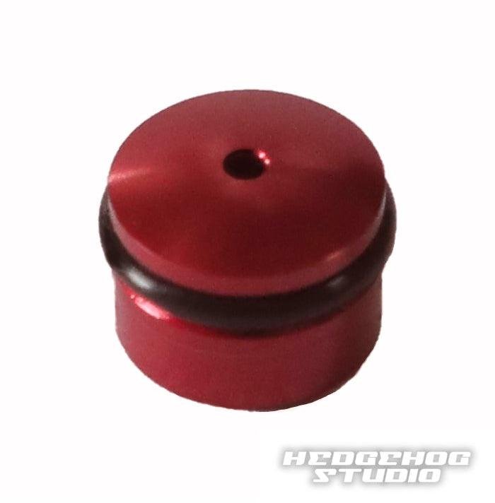 Eine kleine, runde, rote Hedgehog Studio Knob Cap aus Duraluminium mit zentralem Loch und schwarzem Ring, entworfen für Daiwa Finesse Knobs. Mit dem Hedgehog Studio Logo in der unteren rechten Ecke.