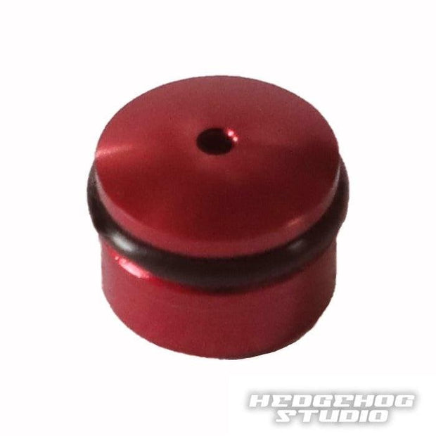 Eine kleine, runde, rote Hedgehog Studio Knob Cap aus Duraluminium mit zentralem Loch und schwarzem Ring, entworfen für Daiwa Finesse Knobs. Mit dem Hedgehog Studio Logo in der unteren rechten Ecke.