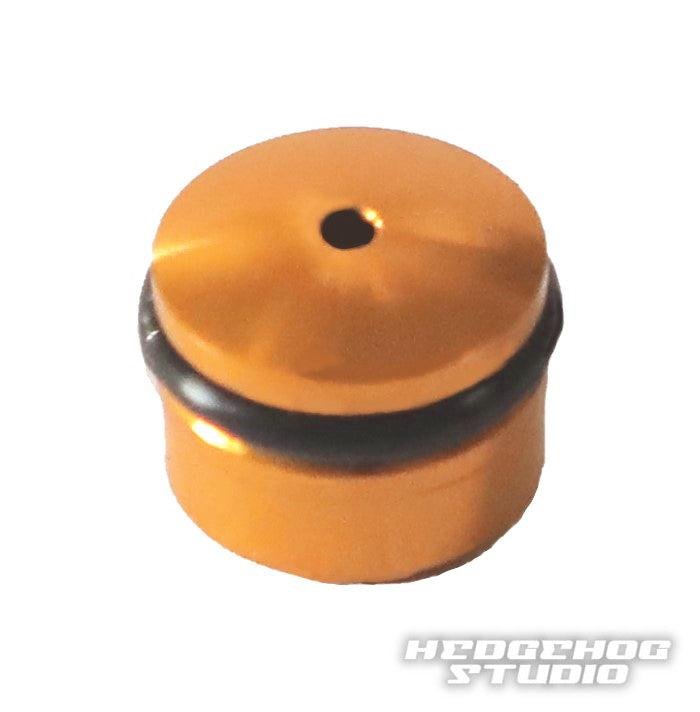 Eine kleine, zylindrische, orangefarbene Hedgehog Studio Knob-Kappe für den Daiwa Finesse Knob mit zentralem Loch und schwarzem O-Ring auf weißem Hintergrund. In der unteren rechten Ecke erscheint der Text „HEDGEHOG STUDIO“.
