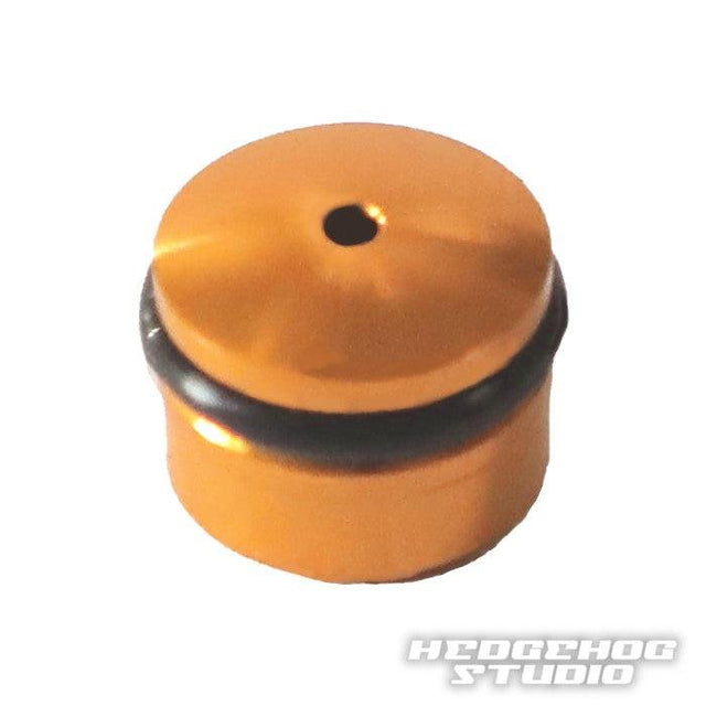 Eine kleine, zylindrische, orangefarbene Hedgehog Studio Knob-Kappe für den Daiwa Finesse Knob mit zentralem Loch und schwarzem O-Ring auf weißem Hintergrund. In der unteren rechten Ecke erscheint der Text „HEDGEHOG STUDIO“.