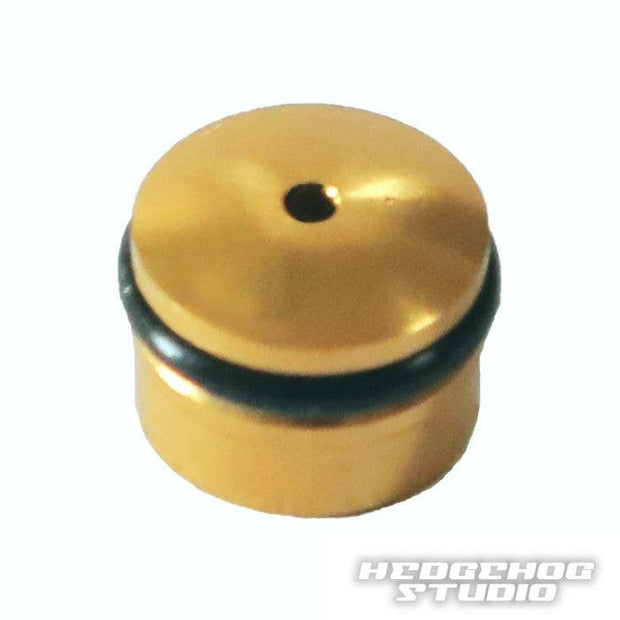 Die Hedgehog Studio Knob Cap für Daiwa Finesse Knobs ist ein kleines, rundes, goldenes Duraluminium-Bauteil mit einem zentralen Loch, einem schwarzen O-Ring und dem Hedgehog Studio-Logo – perfekt zum Aufrüsten Ihrer Angelrolle oder Daiwa Finesse Knobs.